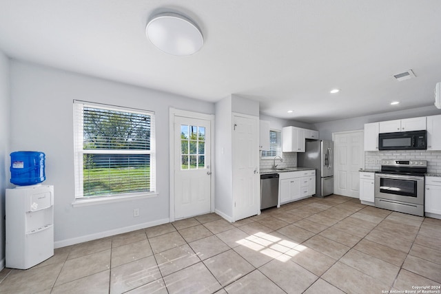 kitchen with light tile patterned floors, backsplash, stainless steel appliances, and white cabinetry