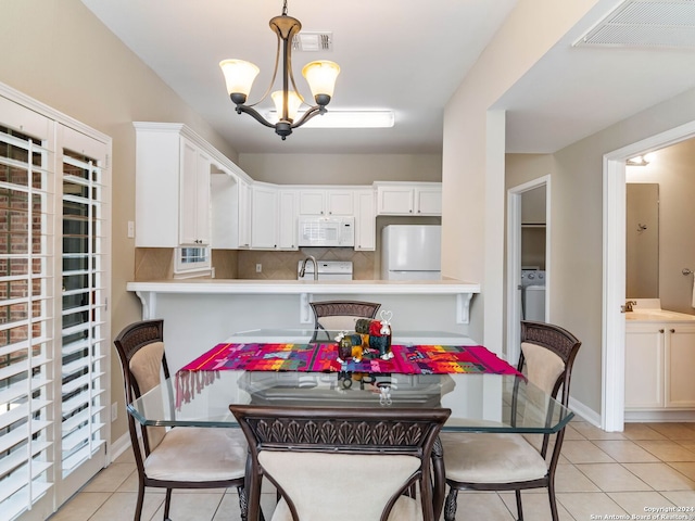 tiled dining room with sink, a chandelier, and washer / dryer