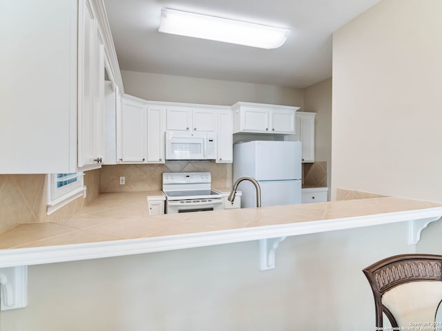 kitchen featuring white cabinets, a kitchen breakfast bar, white appliances, and kitchen peninsula