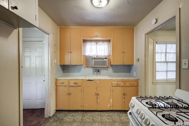 kitchen with gas range gas stove, sink, backsplash, tile countertops, and a textured ceiling