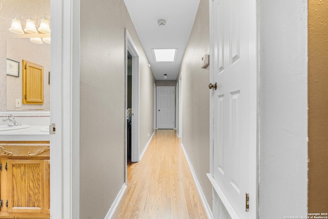 hall featuring light wood finished floors, a sink, and baseboards