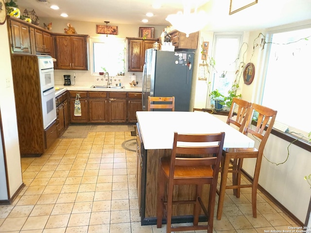 kitchen featuring white double oven, backsplash, sink, light tile patterned floors, and stainless steel refrigerator