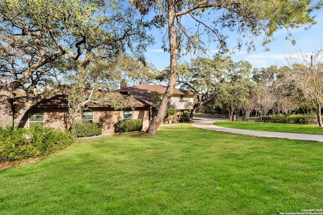 view of front of house featuring concrete driveway, a front lawn, a chimney, and brick siding