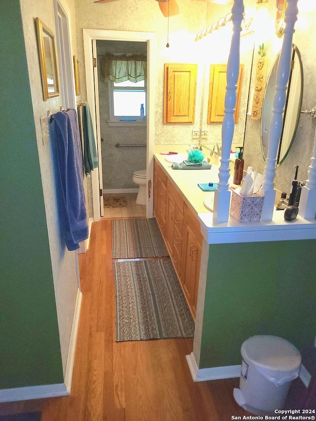 bathroom featuring double vanity, wood finished floors, toilet, and baseboards