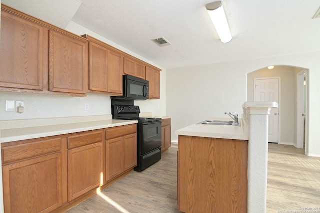 kitchen with sink, black appliances, a center island with sink, and light hardwood / wood-style floors