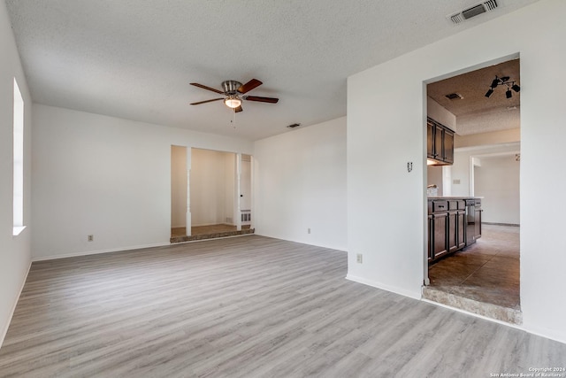 empty room with a textured ceiling, light wood-type flooring, and ceiling fan