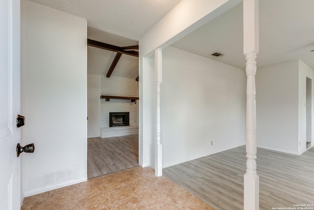 spare room featuring vaulted ceiling with beams, a textured ceiling, light hardwood / wood-style floors, and a brick fireplace