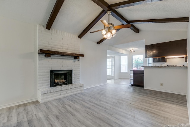 unfurnished living room with ceiling fan, a brick fireplace, light hardwood / wood-style flooring, lofted ceiling with beams, and a textured ceiling