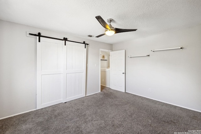 unfurnished bedroom featuring carpet, ceiling fan, a barn door, and a closet