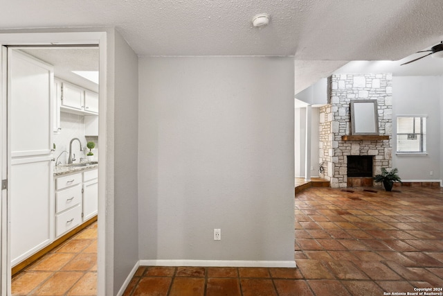 unfurnished living room with ceiling fan, a fireplace, a textured ceiling, and sink