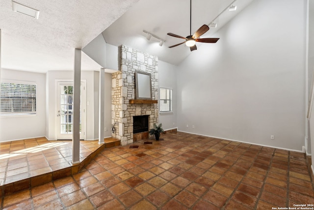 unfurnished living room featuring high vaulted ceiling, track lighting, ceiling fan, a textured ceiling, and a fireplace