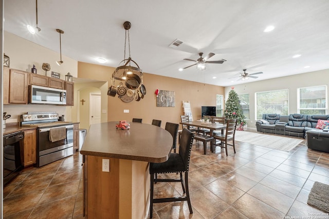 kitchen featuring pendant lighting, a kitchen breakfast bar, ceiling fan, appliances with stainless steel finishes, and a kitchen island