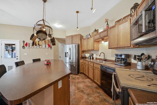 kitchen with appliances with stainless steel finishes, dark tile patterned floors, sink, a center island, and hanging light fixtures