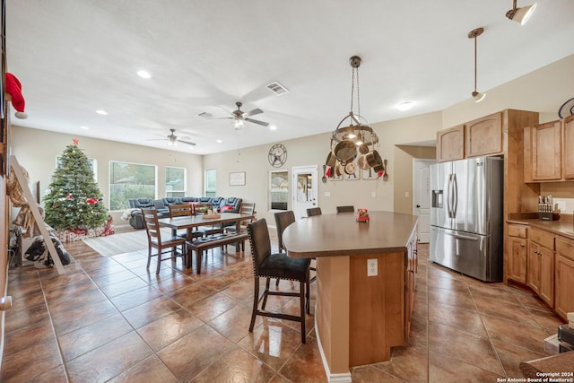 kitchen with a kitchen bar, stainless steel refrigerator with ice dispenser, ceiling fan, pendant lighting, and a center island