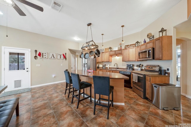 kitchen with stainless steel appliances, ceiling fan, sink, pendant lighting, and a kitchen island