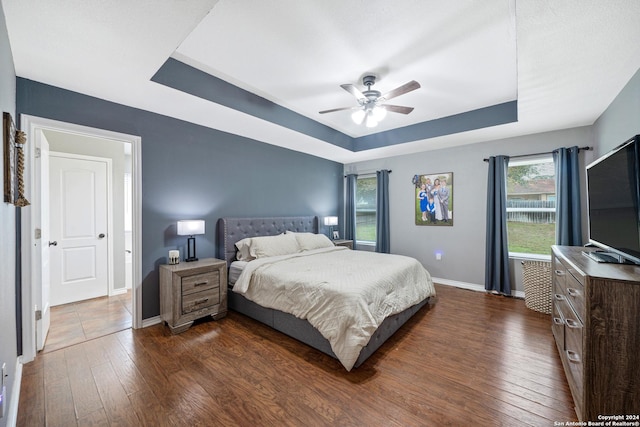 bedroom with a raised ceiling, ceiling fan, and dark hardwood / wood-style flooring