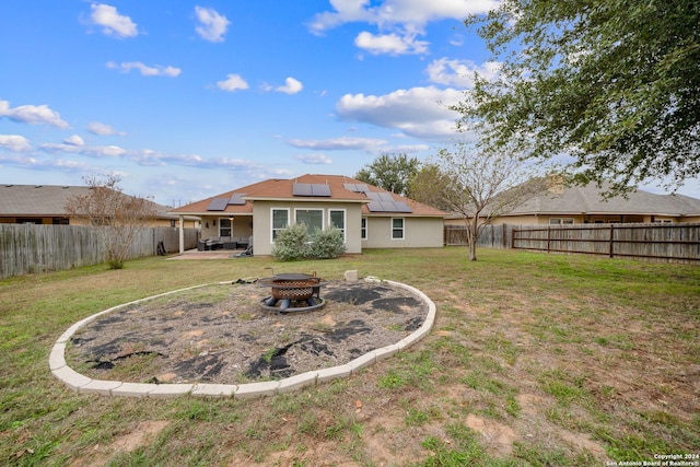 back of property featuring solar panels, a patio, an outdoor fire pit, and a lawn