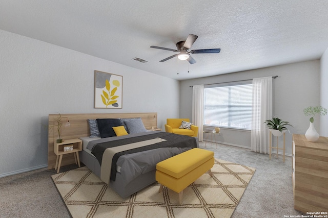 bedroom with ceiling fan, light colored carpet, and a textured ceiling