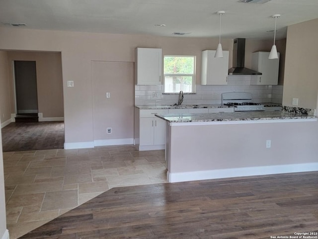 kitchen featuring wall chimney range hood, hanging light fixtures, white gas range, light wood-type flooring, and white cabinetry