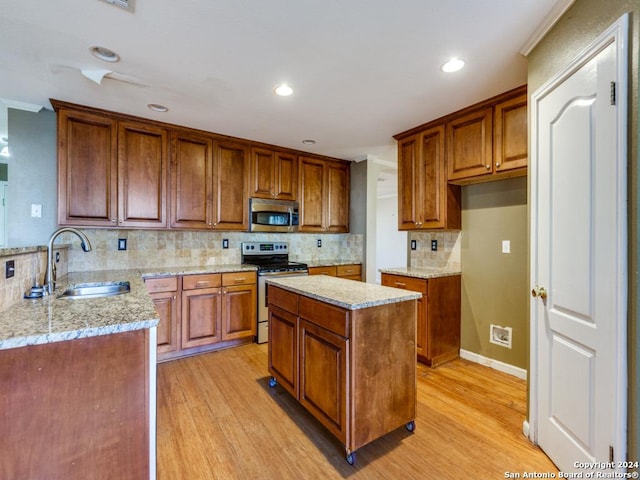 kitchen featuring sink, tasteful backsplash, appliances with stainless steel finishes, a kitchen island, and light wood-type flooring