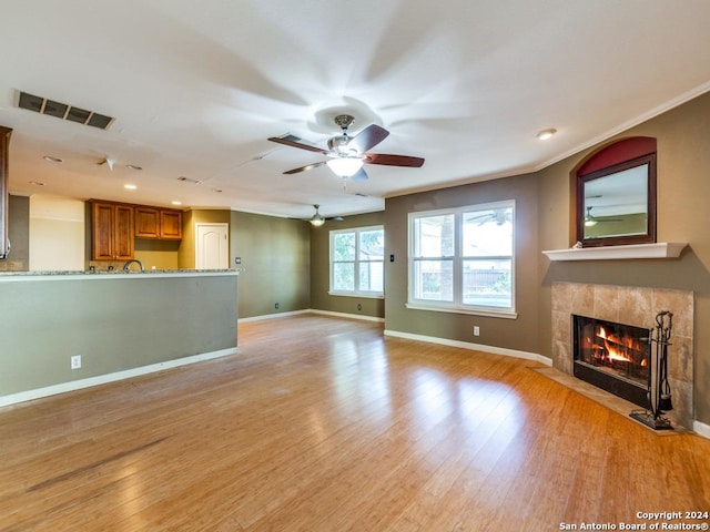 unfurnished living room with ceiling fan, a tiled fireplace, crown molding, and light hardwood / wood-style flooring