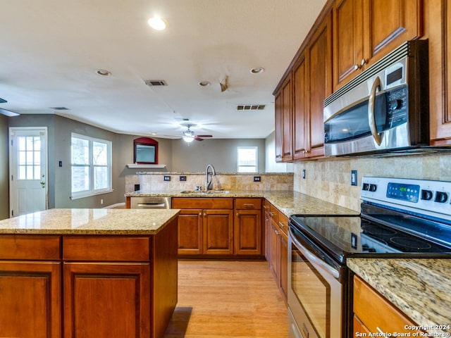 kitchen with kitchen peninsula, appliances with stainless steel finishes, light wood-type flooring, light stone countertops, and sink