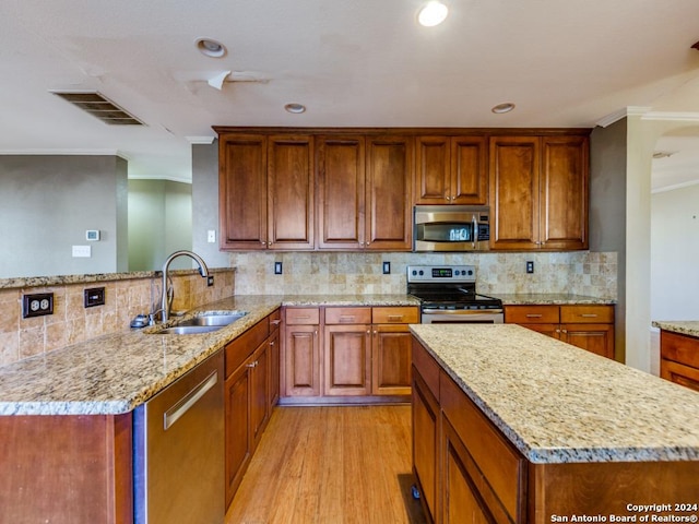 kitchen featuring light stone countertops, appliances with stainless steel finishes, crown molding, sink, and light hardwood / wood-style flooring