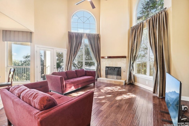 living room with french doors, a towering ceiling, ceiling fan, dark wood-type flooring, and a fireplace