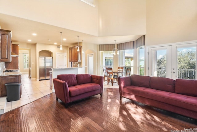 living room featuring light wood-type flooring, french doors, a towering ceiling, and a wealth of natural light