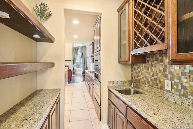 kitchen featuring decorative backsplash, light stone counters, stainless steel appliances, sink, and light tile patterned flooring