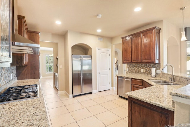 kitchen featuring backsplash, sink, appliances with stainless steel finishes, decorative light fixtures, and light stone counters