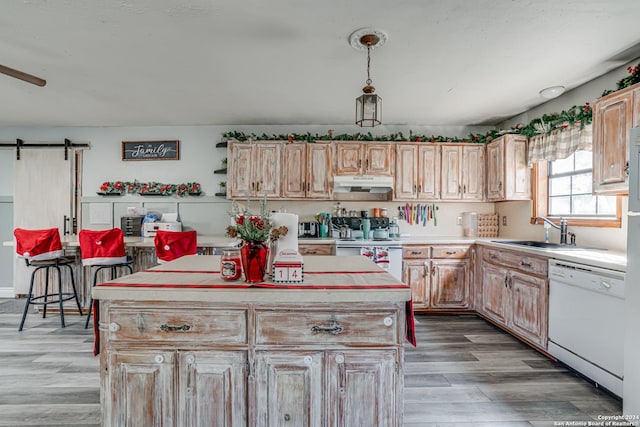 kitchen with a center island, sink, a barn door, decorative light fixtures, and white appliances