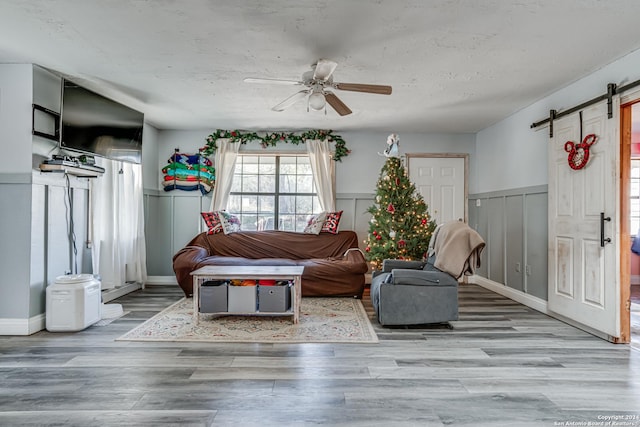 living room featuring ceiling fan, a barn door, and light hardwood / wood-style floors