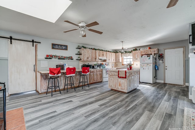 kitchen featuring ceiling fan, a center island, a barn door, light hardwood / wood-style floors, and white appliances