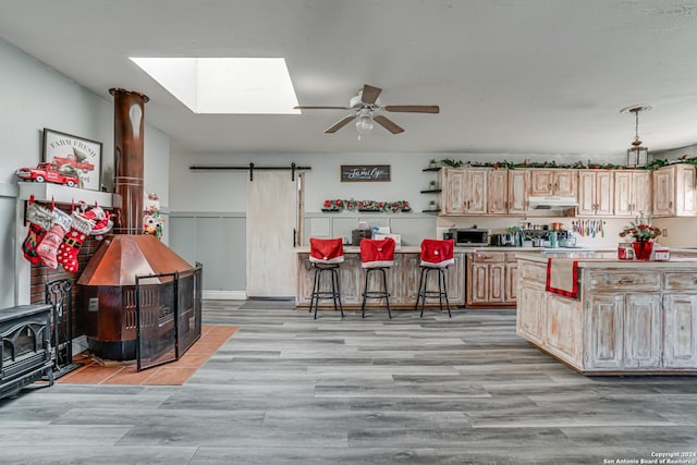 kitchen featuring ceiling fan, light brown cabinets, a barn door, a breakfast bar, and light wood-type flooring