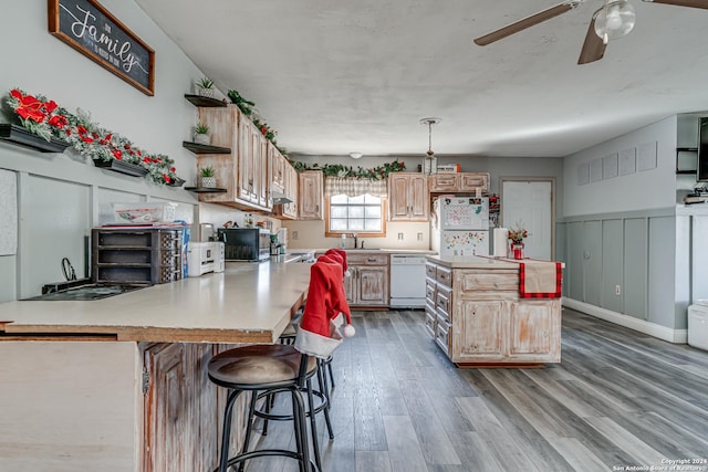 kitchen with pendant lighting, light hardwood / wood-style floors, white appliances, a kitchen bar, and light brown cabinetry