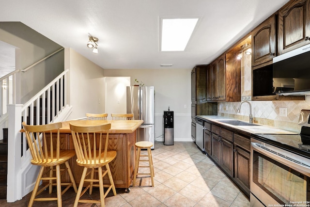 kitchen with appliances with stainless steel finishes, backsplash, a kitchen breakfast bar, dark brown cabinets, and sink