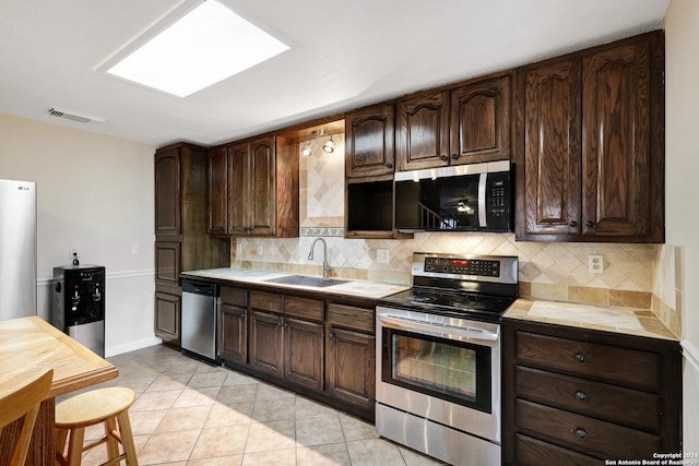 kitchen with dark brown cabinetry, sink, decorative backsplash, light tile patterned floors, and appliances with stainless steel finishes