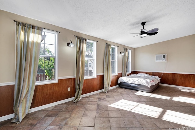 bedroom with a wall mounted air conditioner, ceiling fan, wood walls, and a textured ceiling