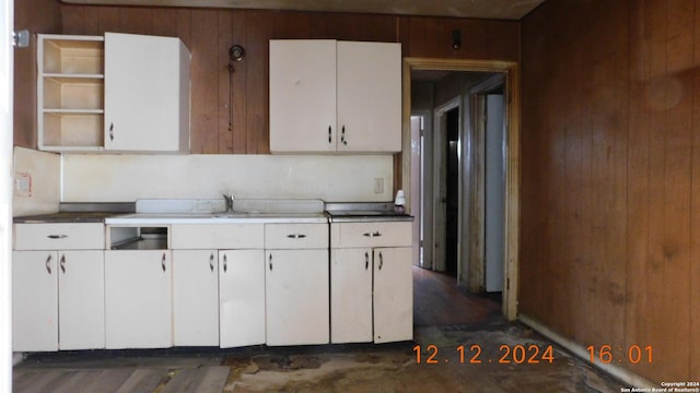 kitchen with white cabinetry, wooden walls, dark wood-type flooring, and sink