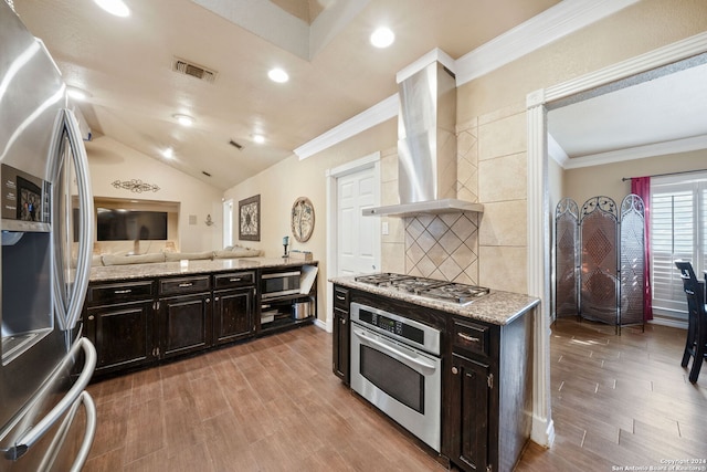 kitchen with wall chimney range hood, vaulted ceiling, hardwood / wood-style flooring, ornamental molding, and stainless steel appliances