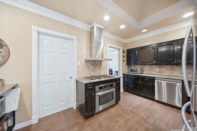 kitchen featuring backsplash, wall chimney exhaust hood, light wood-type flooring, and stainless steel appliances