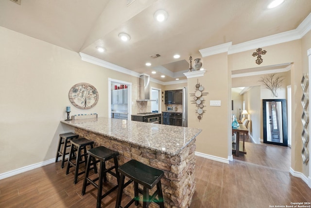 kitchen with kitchen peninsula, light wood-type flooring, light stone counters, wall chimney exhaust hood, and crown molding