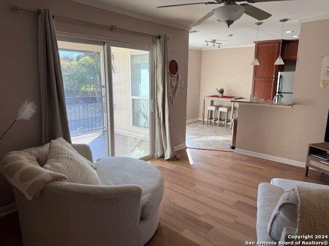 living room with ceiling fan, light wood-type flooring, and crown molding