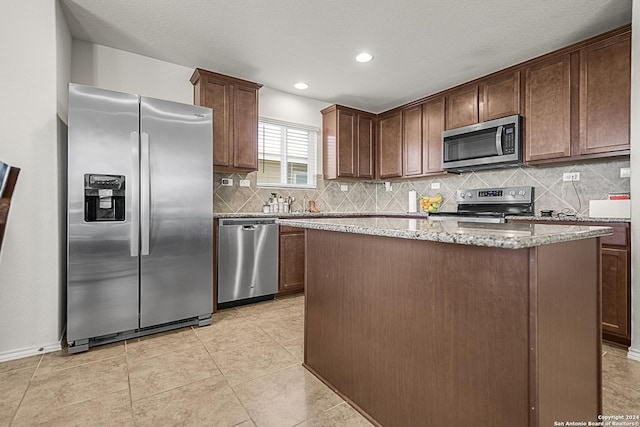 kitchen with light stone countertops, stainless steel appliances, decorative backsplash, dark brown cabinets, and a kitchen island