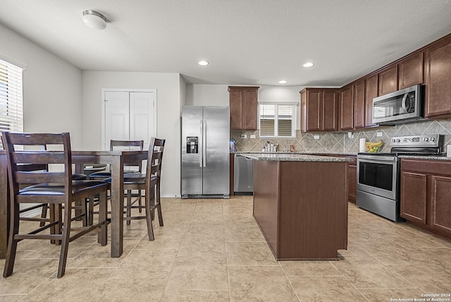 kitchen with dark brown cabinetry, a center island, stainless steel appliances, a textured ceiling, and decorative backsplash