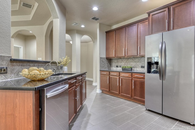 kitchen with decorative backsplash, appliances with stainless steel finishes, a textured ceiling, sink, and dark stone countertops