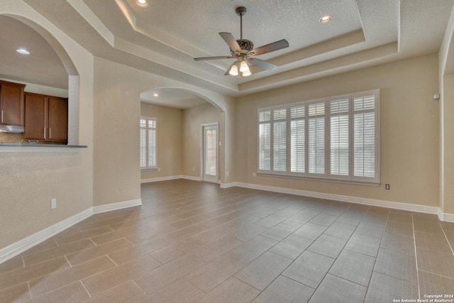 unfurnished room featuring ceiling fan, a raised ceiling, and a textured ceiling