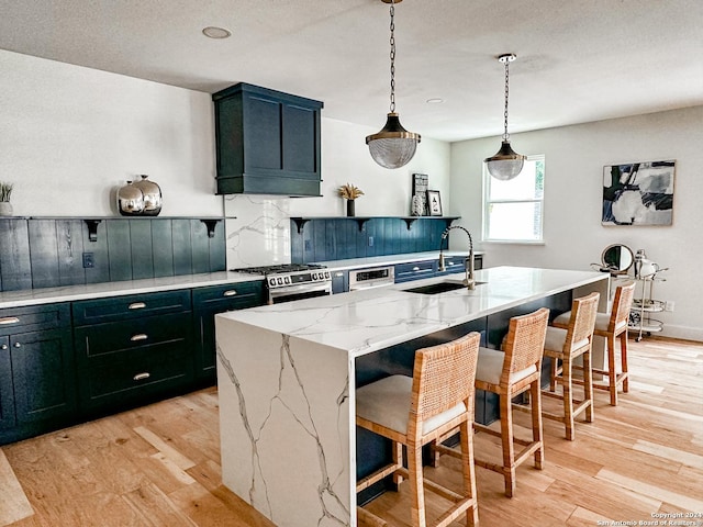 kitchen featuring gas range, sink, a kitchen breakfast bar, a kitchen island with sink, and light wood-type flooring