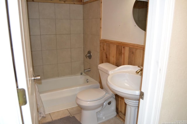 bathroom featuring tile patterned flooring, tiled shower / bath combo, wood walls, and toilet